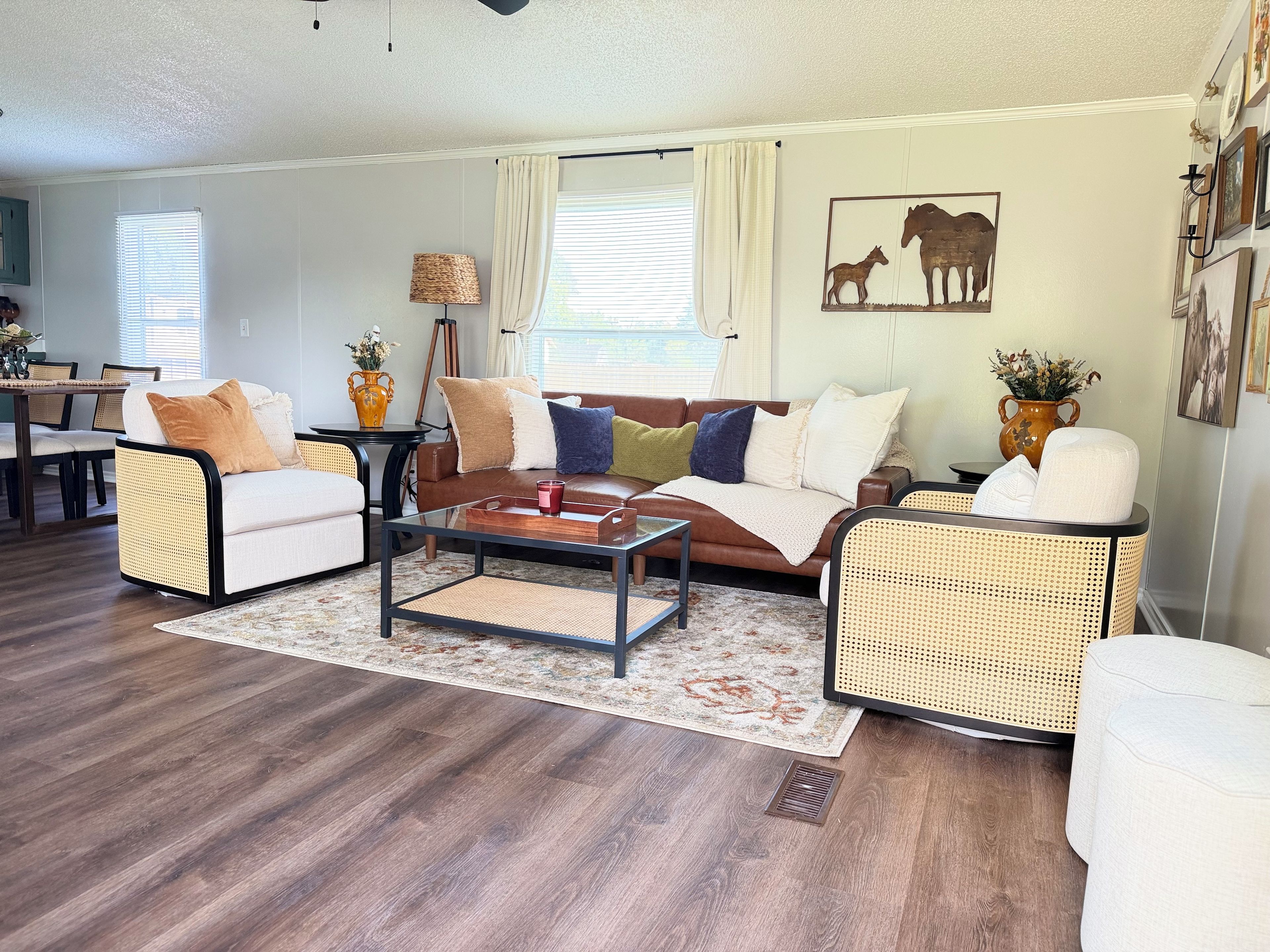 A living room with a brown leather sofa, two wicker armchairs, a glass coffee table, and a dining area with a wooden table and chairs.