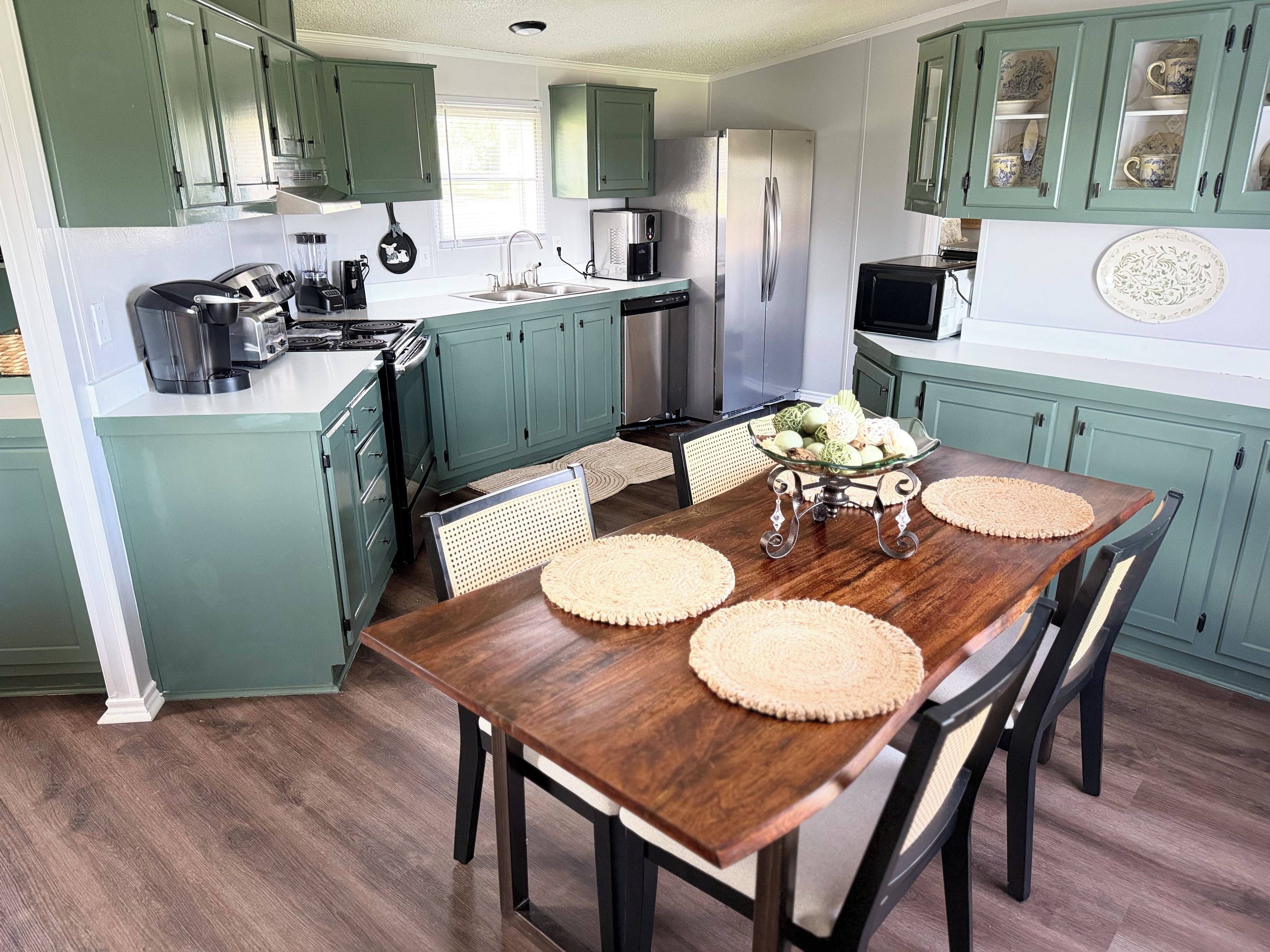 A kitchen with teal cabinets, a wooden dining table with placemats, and a refrigerator.