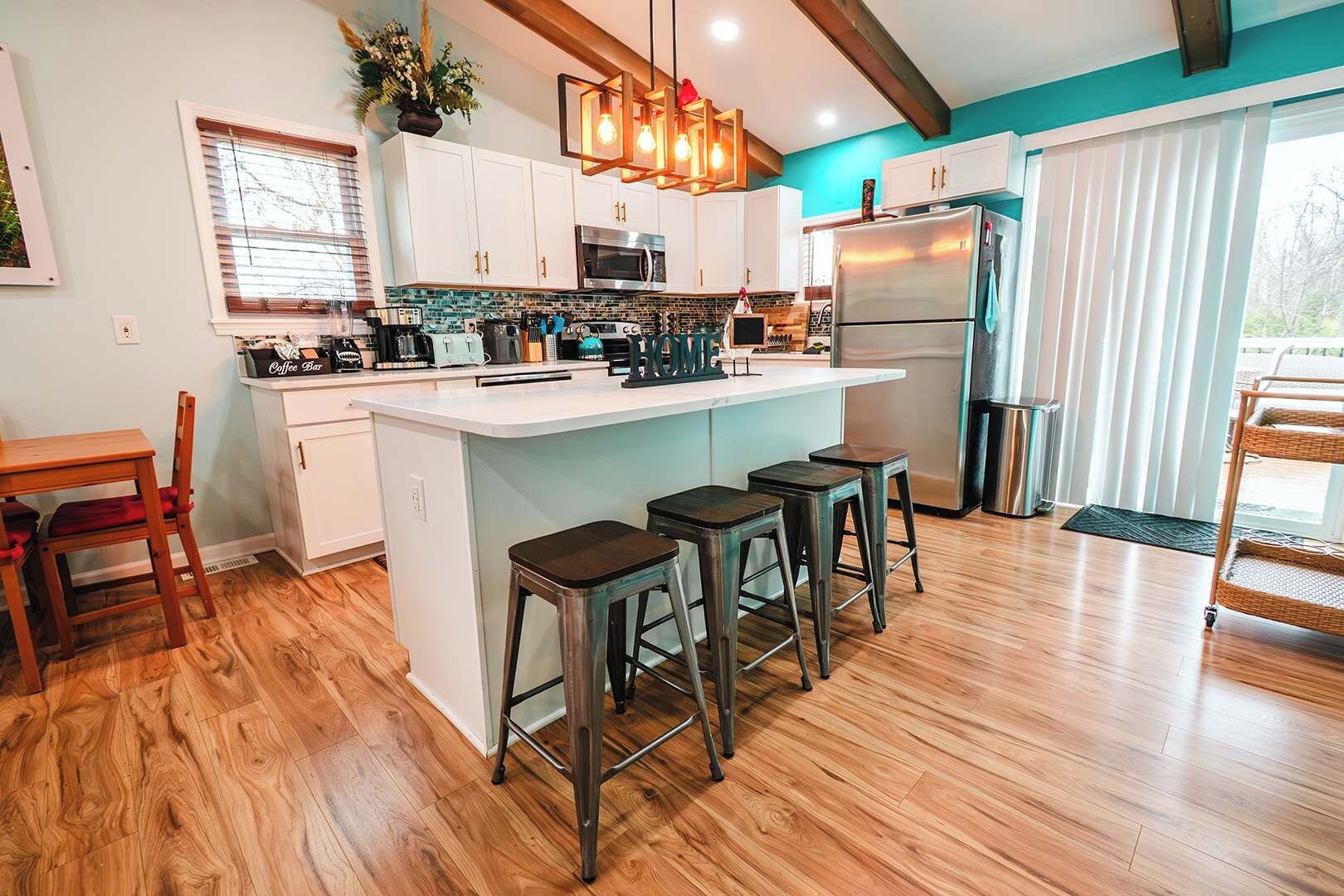 Una cocina moderna con una isla central, taburetes de bar, un refrigerador y un comedor con una silla y mesa.