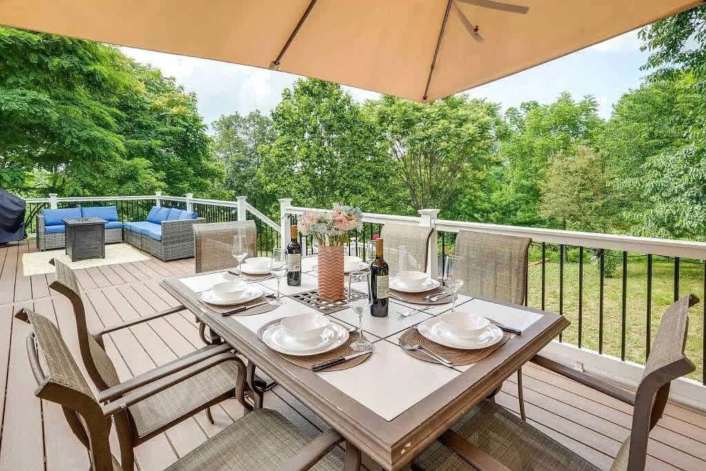 Un área de comedor al aire libre con terraza de madera, una mesa dispuesta para cuatro personas y vistas de la vegetación circundante.
