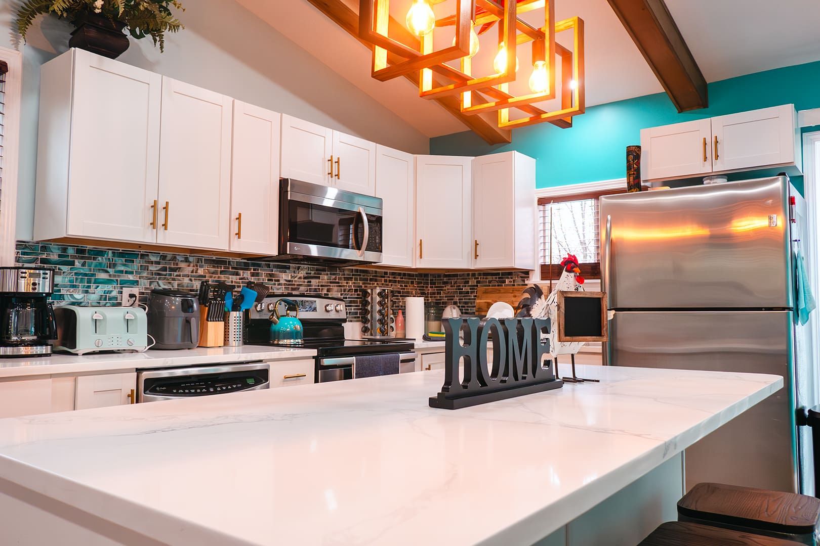 A modern kitchen with white cabinets, a stainless steel refrigerator, a built-in oven, and a large island with a sink.