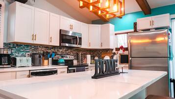 A modern kitchen with white cabinets, a stainless steel refrigerator, a built-in oven, and a large island with a sink.