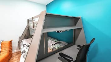 A bunk bed with a desk and chair, a blue wall, and an orange cushion.