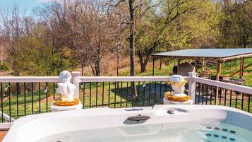 A hot tub with two statues, a pergola, and a view of trees and grass.