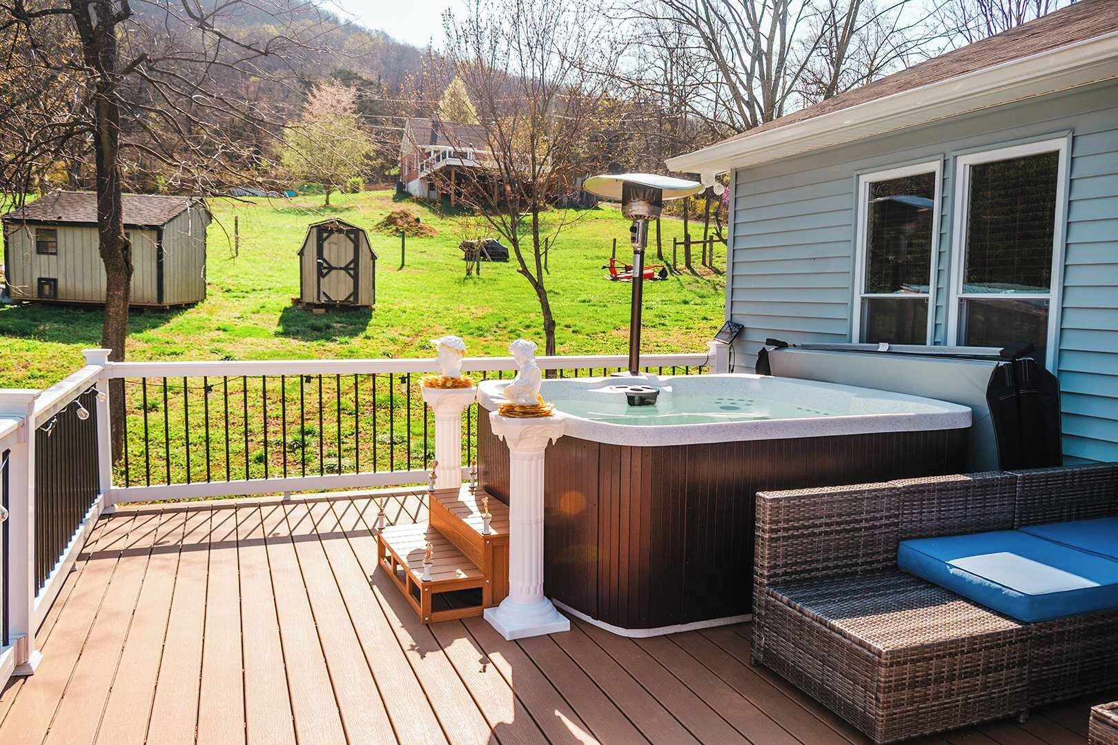 Une terrasse dotée d’un jacuzzi, de meubles en osier et offrant une vue sur un paysage verdoyant.