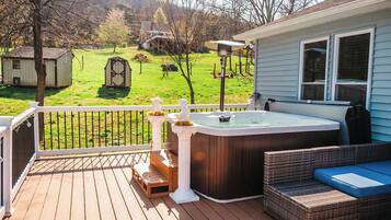 A deck with a hot tub, wicker furniture, and a view of a green landscape.