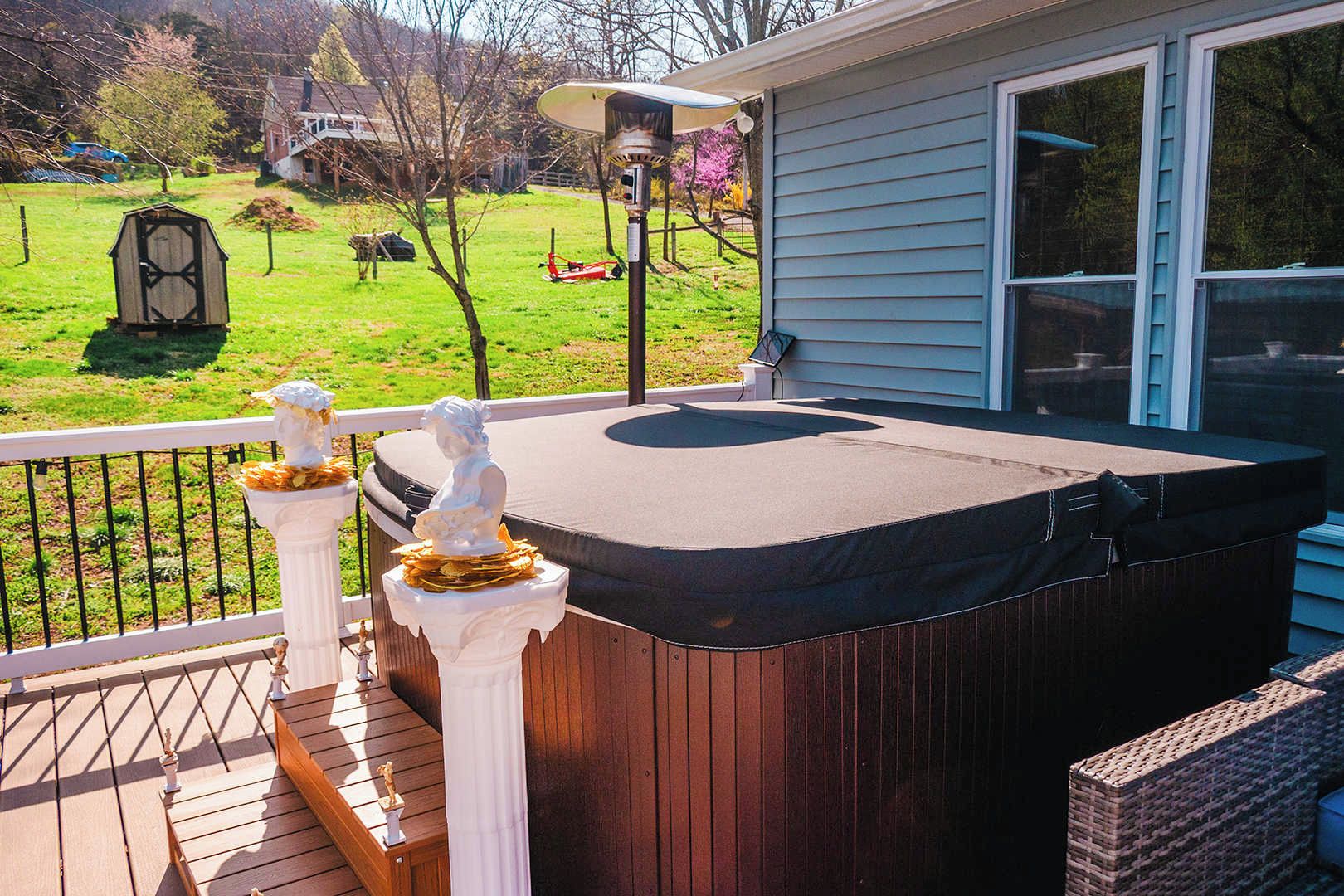 Een hottub op een houten terras met een reling, een standbeeld en een huis op de achtergrond.