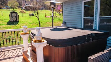 Een hottub op een houten terras met een reling, een standbeeld en een huis op de achtergrond.