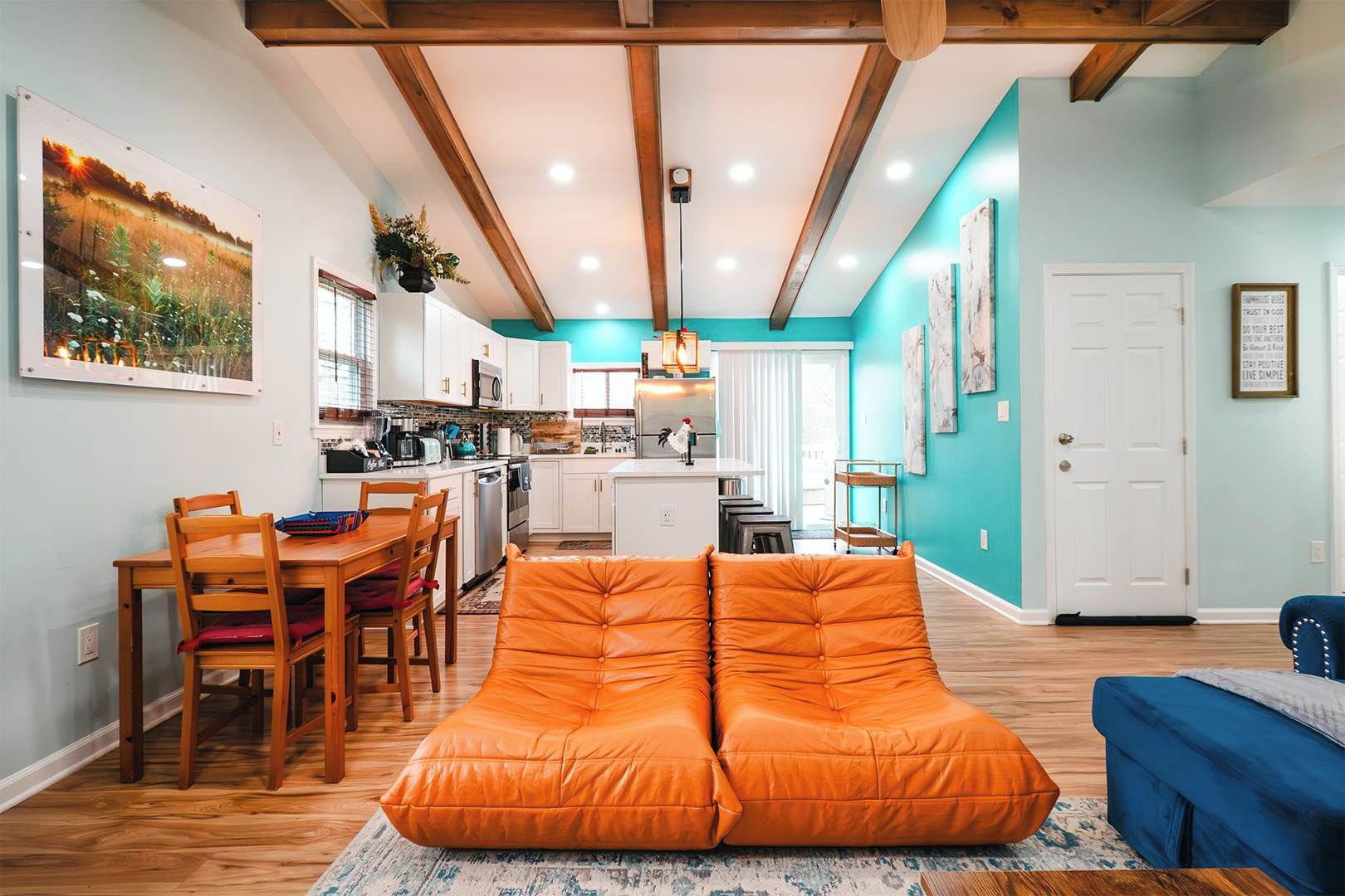 Een moderne keuken met witte kastjes, een eethoek met houten stoelen en een vrolijke teal accentmuur.