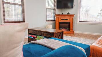 A living room with a fireplace, a television mounted above it, and a sofa with a blue cover.