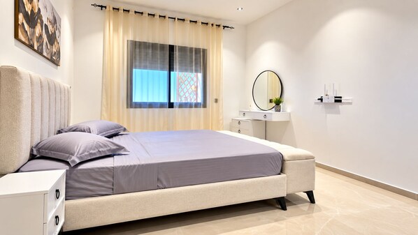 Un dormitorio moderno con una cama, mesitas de noche, un espejo y una ventana con cortinas.