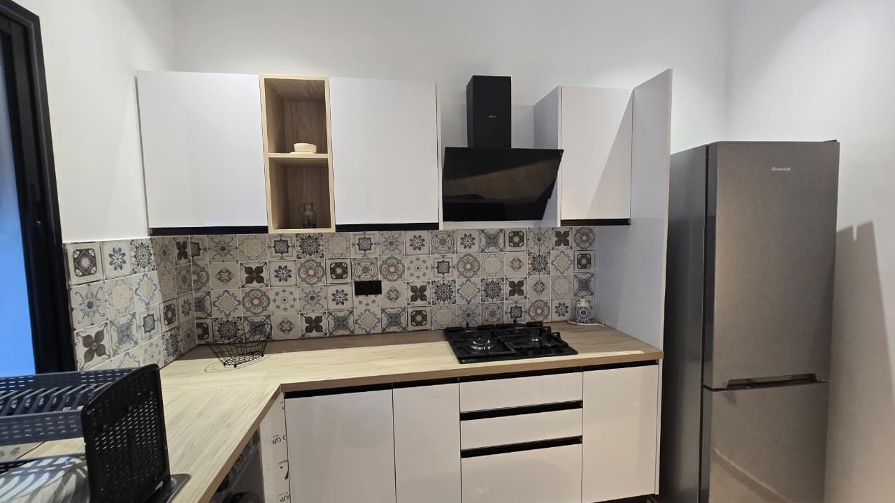 Een kleine keuken met een ingebouwde gasplaat, een koelkast en witte kasten.