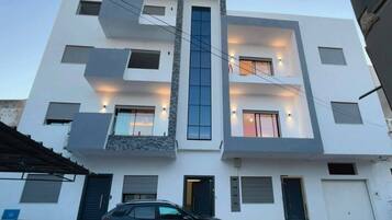 A multi-story building with a modern design, featuring a central staircase, multiple windows with external lighting, and a car parked in front.