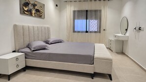A modern bedroom with a bed, nightstands, a dresser, and a window with curtains.