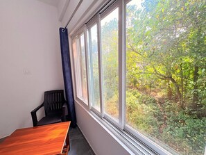 A room with a wooden table and a black chair, a window with a view of a forest, and a power outlet on the wall. - Room-studio Couple Choice R -10 1st Floo (Arambol)
