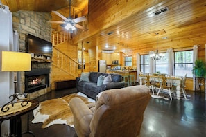 A cozy cabin interior with a stone fireplace, a sofa, a dining area, and a kitchen. - Honey Bear - 1BR Cabin & Hot Tub (Broken Bow)