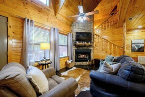 A cozy cabin interior with a stone fireplace, wooden walls, a ceiling fan, and a comfortable seating area. - Honey Bear - 1BR Cabin & Hot Tub (Broken Bow)