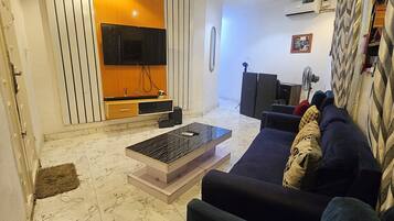 A modern living room with a sofa, a coffee table, a TV, and a fan.