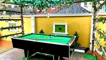 A pool table in a covered outdoor area with a yellow wall and a small window.
