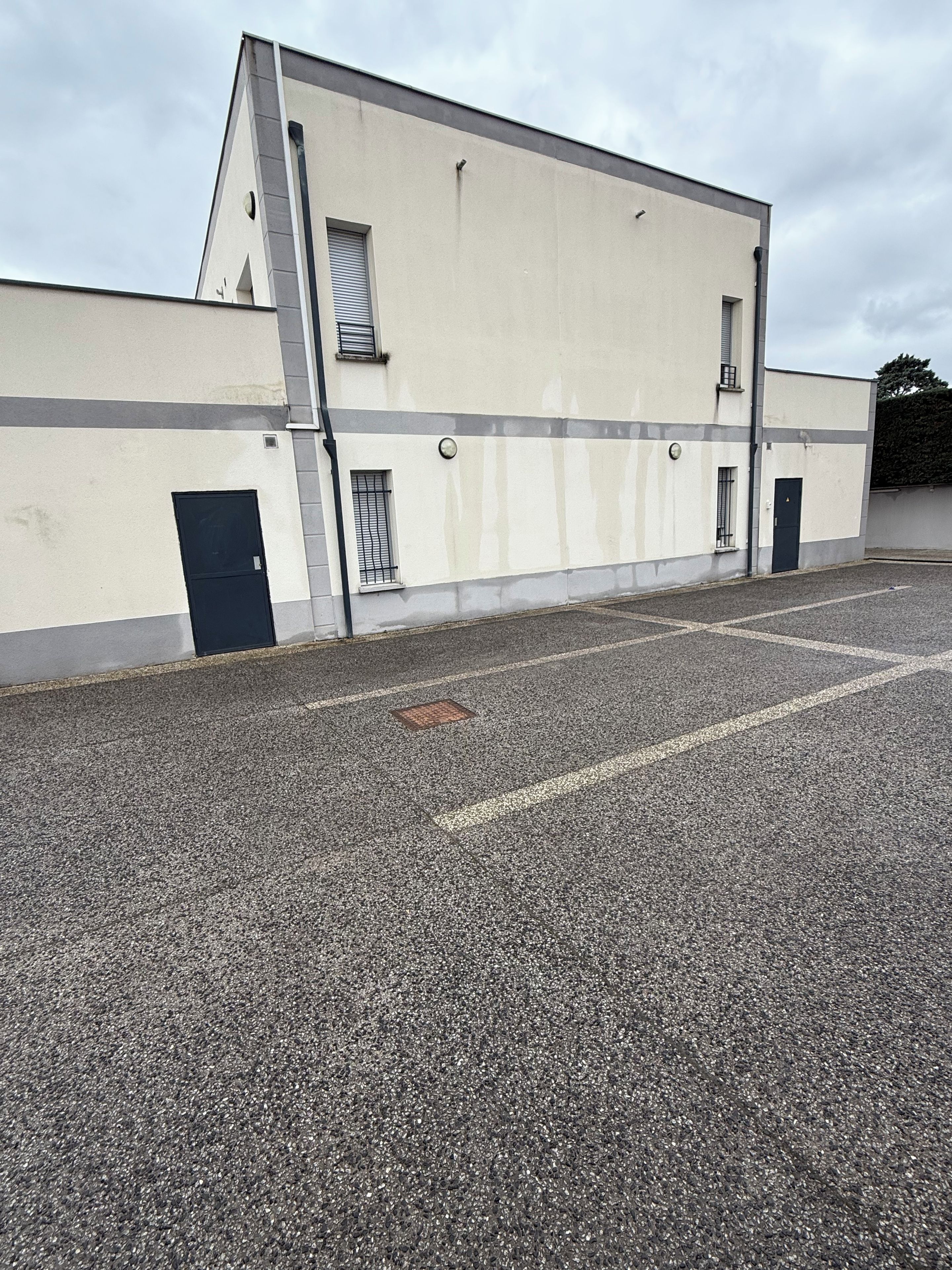 A building with a flat facade, a parking lot, and a gated entrance.