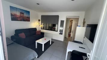 A compact living space with a sofa, a small table, a TV, and a window.