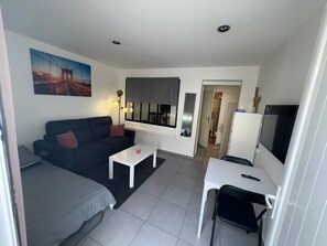Ein gemütlicher, kleiner Wohnraum mit einer Couch, einem Tisch, einem Fernseher und einem Fenster.