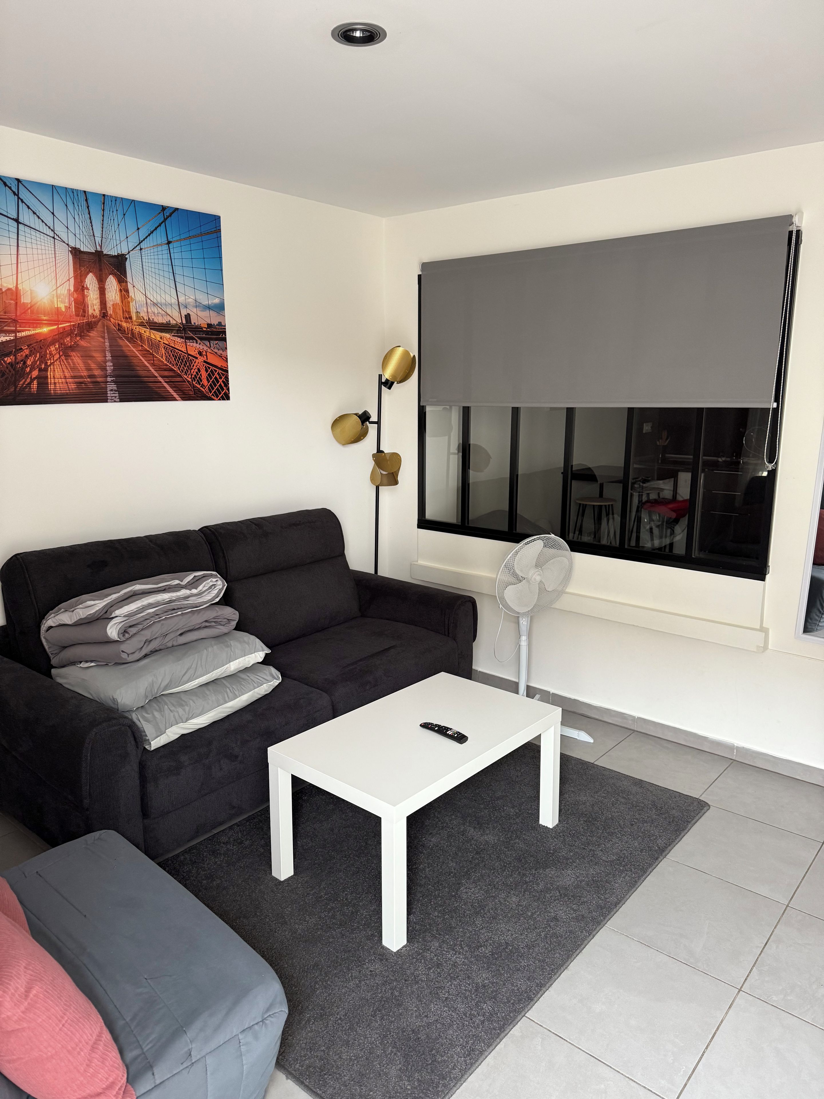 A modern living room with a black sofa, a white coffee table, and a large window with a view of a bridge.
