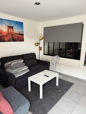 Ein modernes Wohnzimmer mit einer schwarzen Couch, einem weißen Couchtisch und einem großen Fenster mit Blick auf eine Brücke.