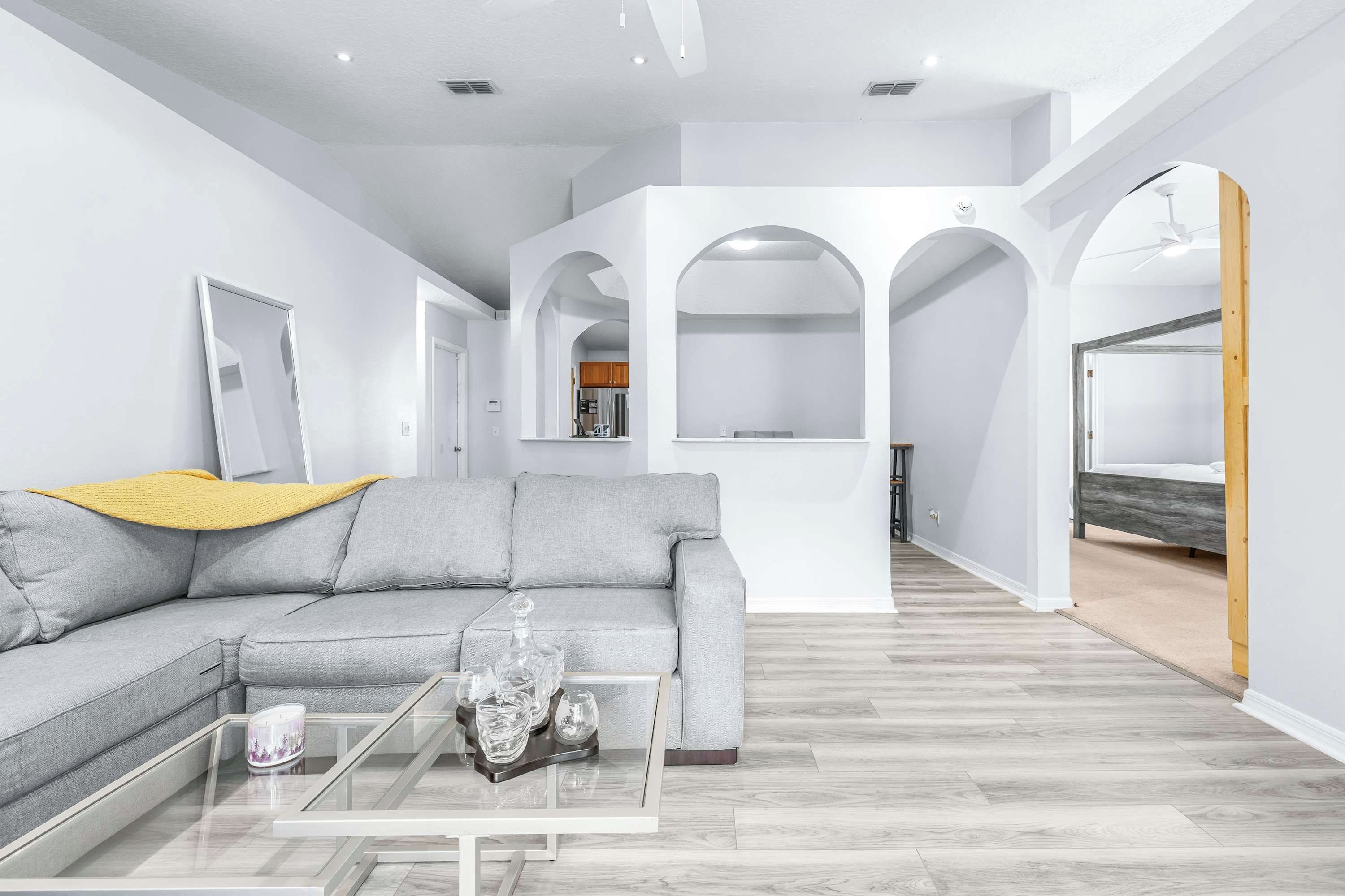 Ein modernes Wohnzimmer mit einem grauen Ecksofa, einem Glastisch und einer gelben Decke.