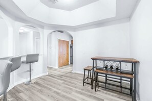 A modern interior with a bar area, seating, and a kitchen in the background. - Cottage on the Bay Pool Home (Tampa)