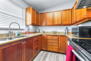 Eine Küche mit Holzausstattung, einer Edelstahl-Spüle, einer Mikrowelle und einem Backofen.
