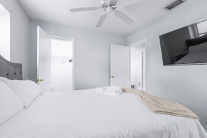 Ein Hotelzimmer mit einem Bett, einem Deckenventilator, einem an der Wand befestigten Fernseher und einer Tür zu einem anderen Raum.