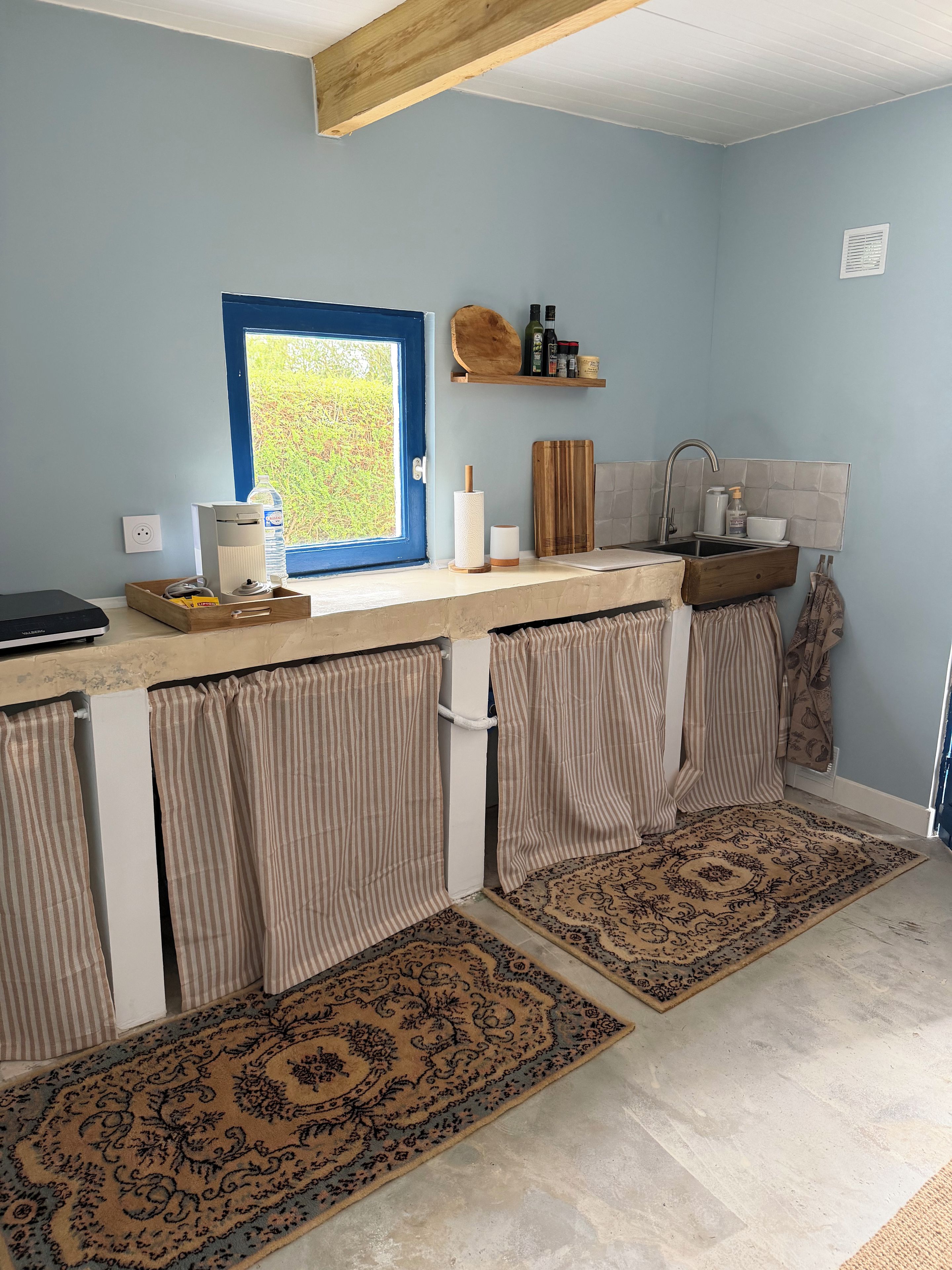 A kitchen with a window, a countertop, a sink, and a wooden shelf.