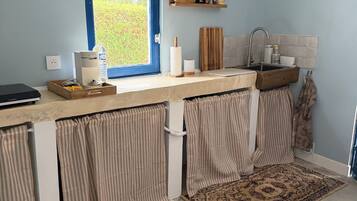 A kitchen with a window, a countertop, a sink, and a wooden shelf.