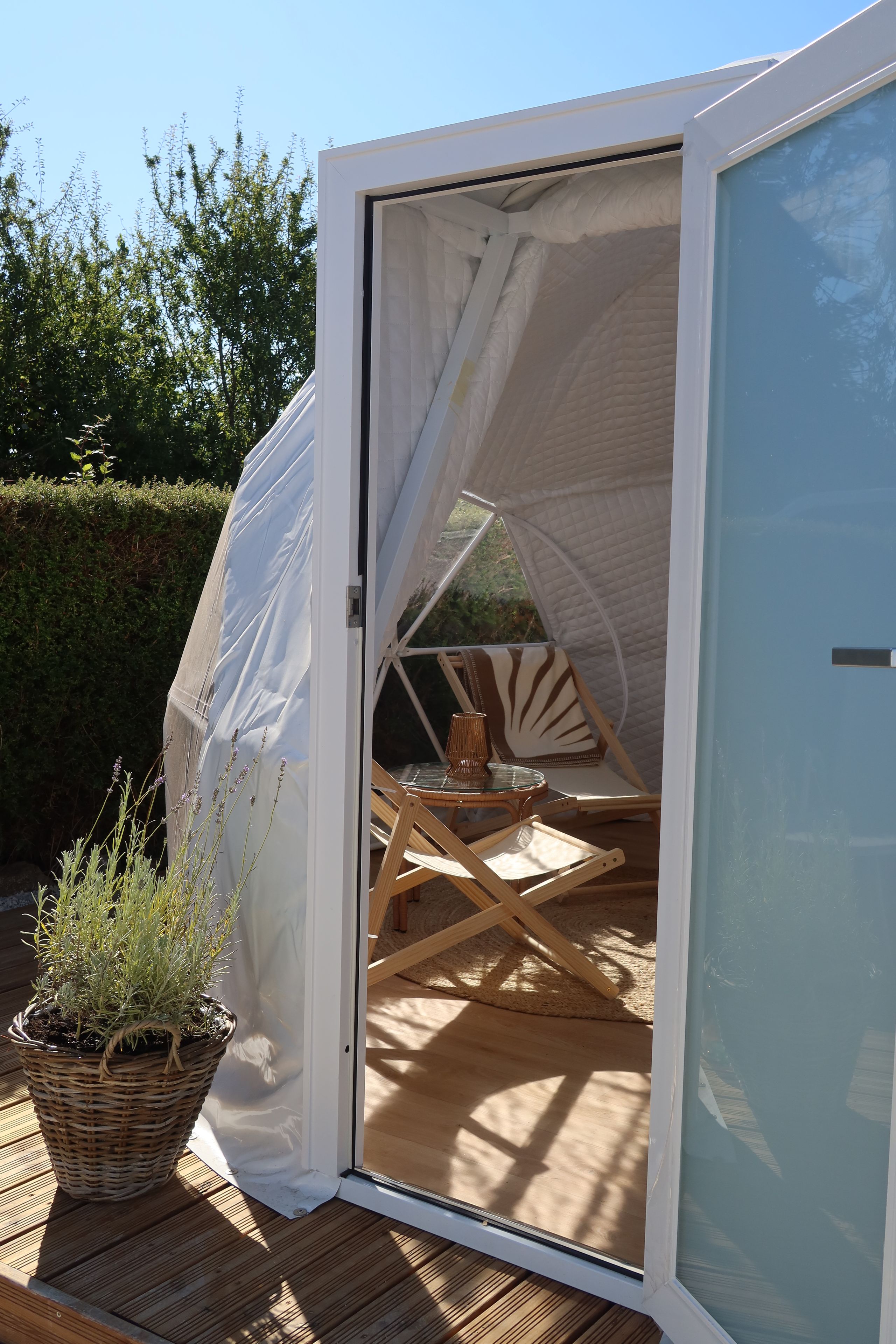 Eine zeltartige Konstruktion mit Glastür, einem Korbwicker-Korb mit Pflanzen und einem Holzterrasse.