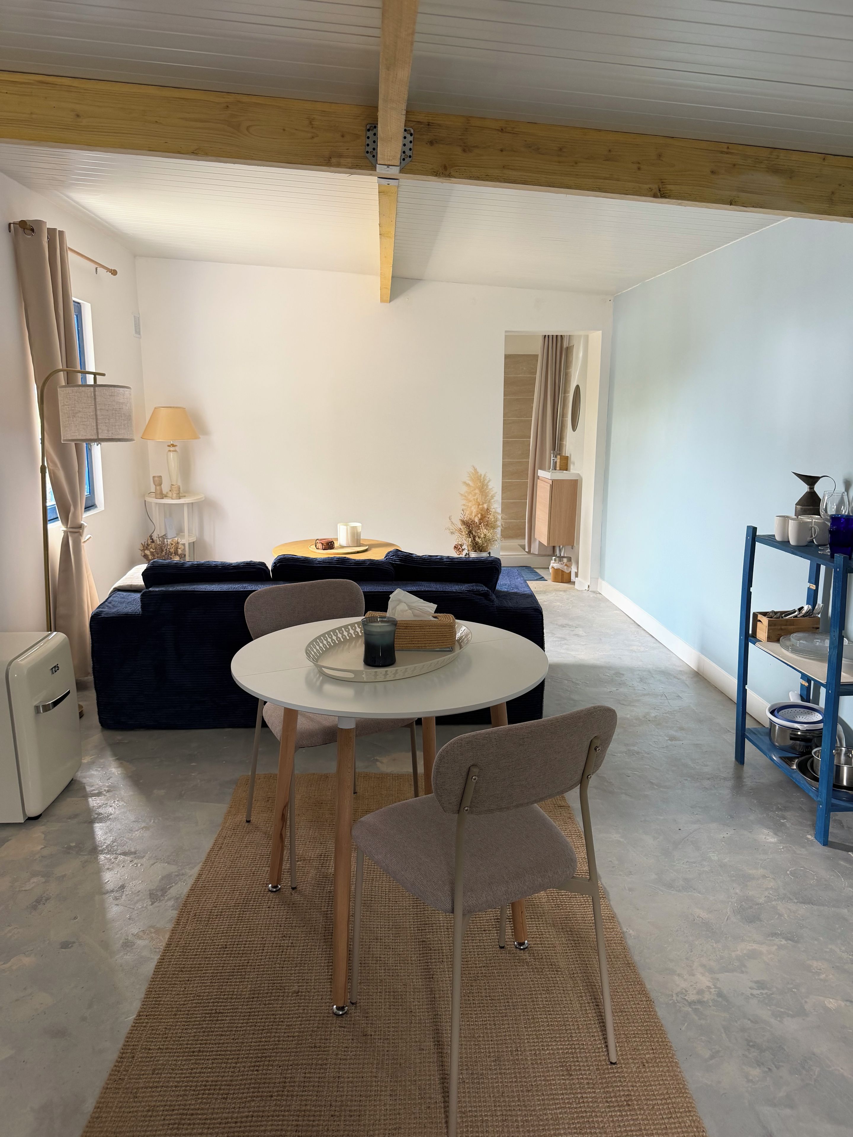 Une pièce comprenant une table ronde, deux chaises, un canapé, une petite table d’appoint avec une lampe et un meuble contenant de l’ustensile de cuisine.