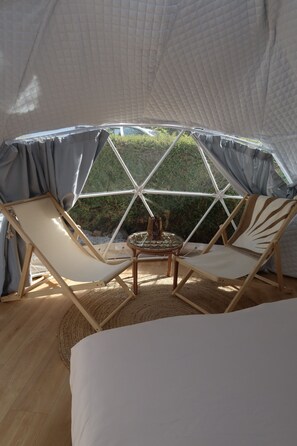 A cozy tent with a bed, two lounge chairs, and a small table.