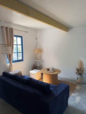 A room with a blue sofa, a round wooden table, a lamp, and a window with curtains.