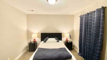 A hotel room with a single bed, two bedside tables, a nightstand, a ceiling light, and a dark curtain.