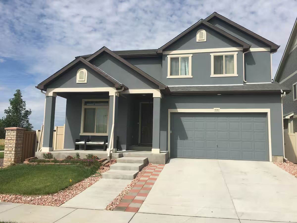 A two-story residential house with a garage, a covered front porch, and a well-maintained lawn.
