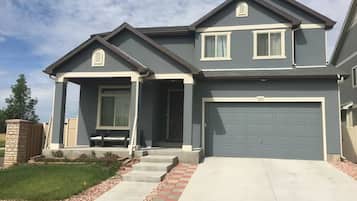 A two-story residential house with a garage, a covered front porch, and a well-maintained lawn.