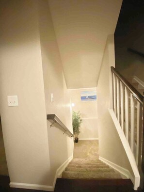 Un escalier avec une rampe, un luminaire fixé au mur et un tableau encadré.