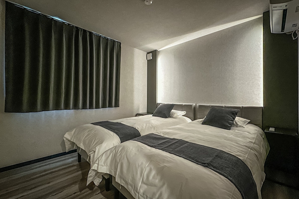 A hotel room with two beds, a large window, and a wall-mounted air conditioning unit.