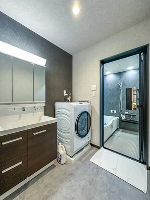 A modern bathroom with a large mirror, a washing machine, and a shower area. - HANASTAY HIRO (Osaka)