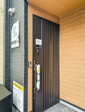 A modern building entrance with a black door, a security camera, and a sign with Japanese text. - HANASTAY HIRO (Osaka)