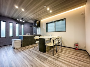 A modern kitchen with a central island, a dining area with a table and chairs, and a window with frosted glass. - HANASTAY HIRO (Osaka)