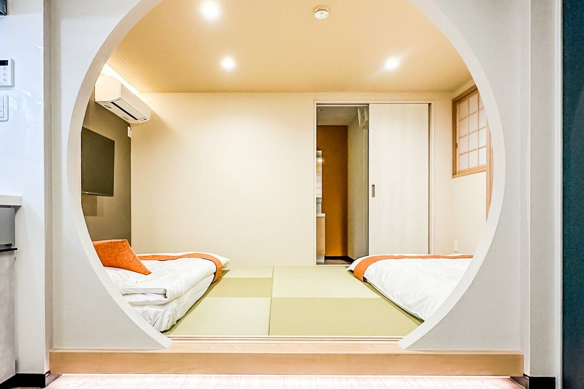 A room with a unique circular window design, a bed with orange bedding, and a wooden floor.
