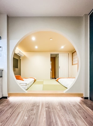 A room with a unique circular window design, a bed with orange bedding, and a wooden floor. - HANASTAY HIRO (Osaka)
