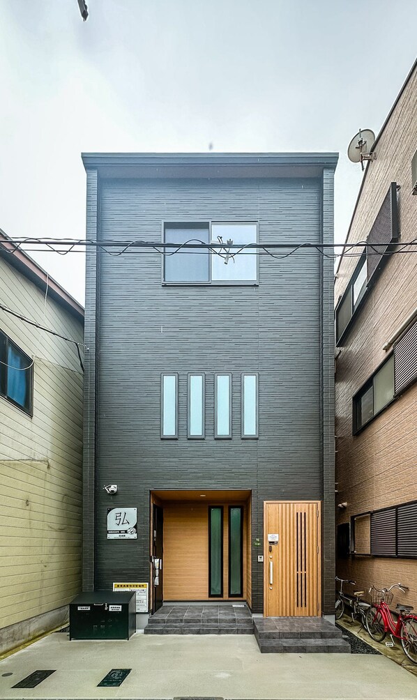 A modern building with a dark facade, a wooden door, and a satellite dish on the roof. - HANASTAY HIRO (Osaka)
