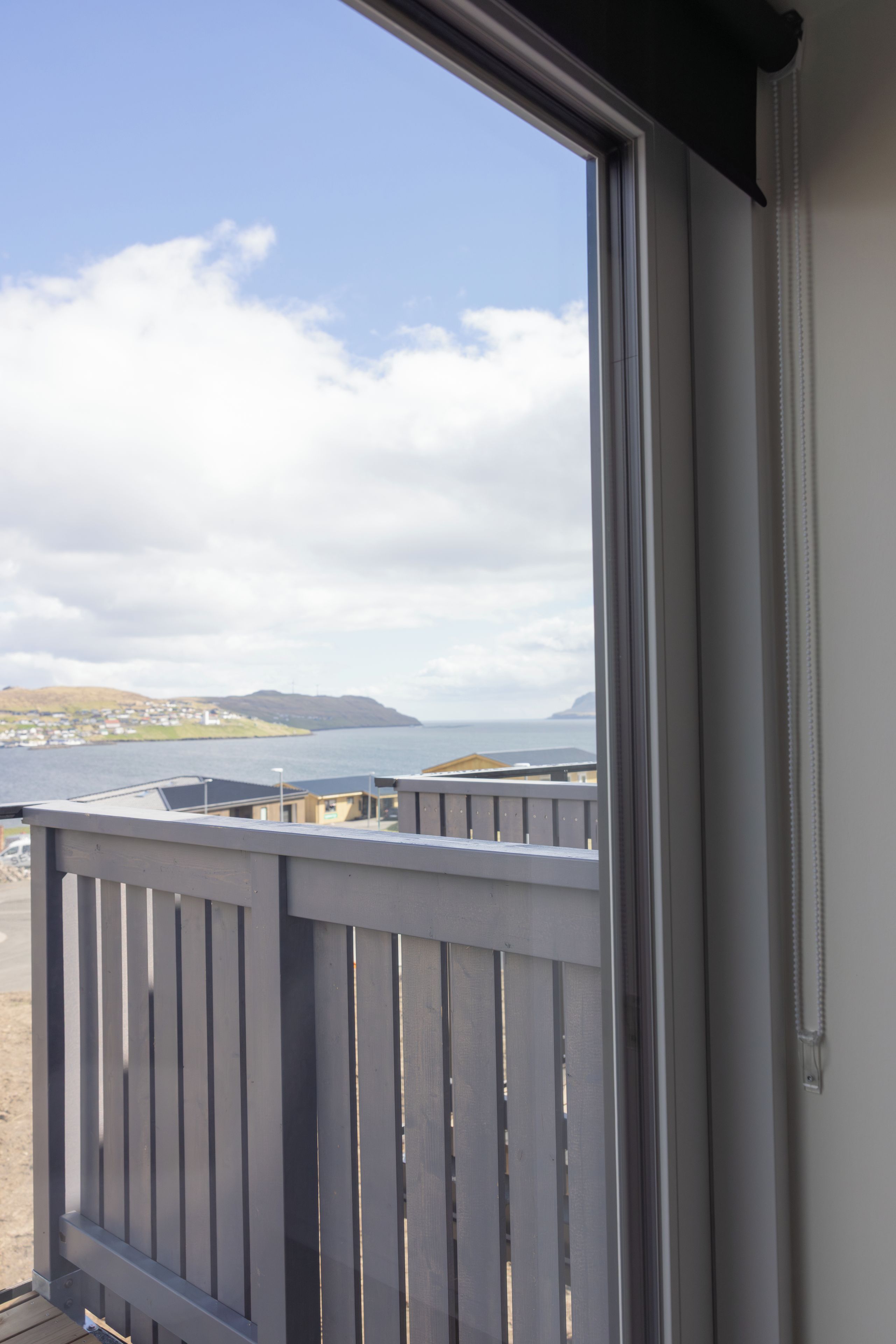 Blick von einem Balkon mit Holzgeländer auf ein Gewässer und entfernte Lande.